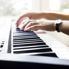 A woman playing piano at the window. A cup of coffee is on the instrument