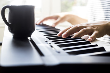 Fototapeta premium A woman playing piano at the window. A cup of coffee is on the instrument