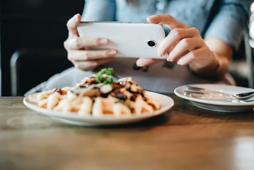 Hands of woman taking a photo of breakfast with smartphone.