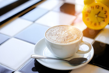 Capuccino coffee and Yellow clock on White and Black Table in Cafe