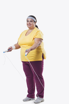 Full length of an overweight female with skipping rope over white background 