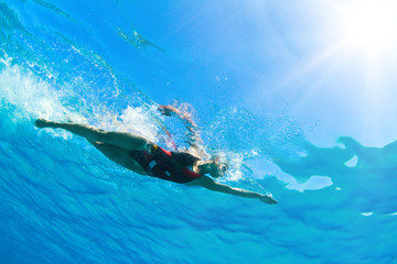 Female professional swimmer gushing through blue Red sea water with bubbles