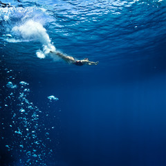professional female swimmer shoutied just after jumping into deep blue ocean with air bubbles trail