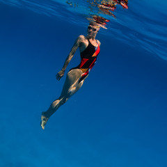 professional sport swimmer floating up underwater in blue with small air bubbles on her face