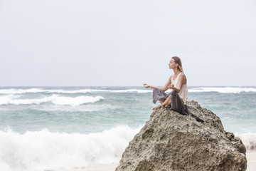 Girl sit at the seaside on the rock and meditating in yoga woman pose