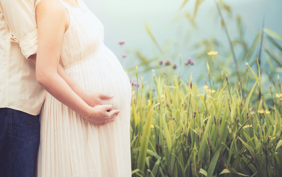 Pregnant woman and her husband hugging on the tummy together in nature outdoor in vintage color tone