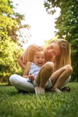 Mother and daughter outdoors in a meadow. Mother and daughter having fun on green grass.