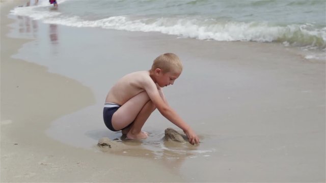 Boy squat on the sea/The boy is playing sand on the coastline