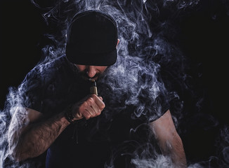 Handsome athletic man is vaping an e-cigarette. Black background. Studio shooting.