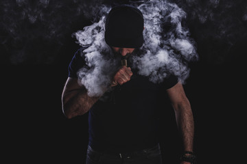 Handsome athletic man is vaping an e-cigarette. Black background. Studio shooting.