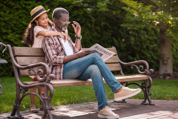 adorable african american granddaughter hugging her grandfather sitting on bench in park
