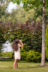 Naklejka premium rear view of little african american girl taking photo of green tree in park