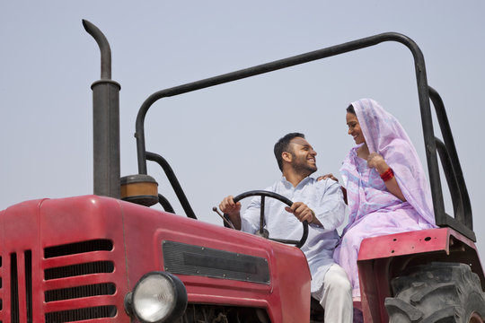 Indian couple looking at each other while sitting in a tractor 