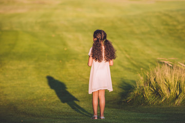 rear view of little african american girl standing on green lawn