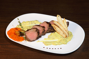 Appetizing steak medium roast, cut into pieces in creamy mushroom sauce. Steak in a white plate on a wooden table.