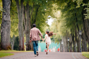 back view of african american girl holding hands with grandfather, jumping and walking in park