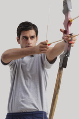 Male archer practicing archery against gray background