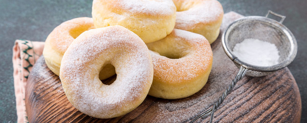 Homemade baked donuts with powdered sugar on green background. Selective focus. Banner.