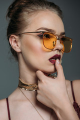 Obraz premium young seductive beautiful woman posing orange sunglasses for fashion shoot, isolated on grey
