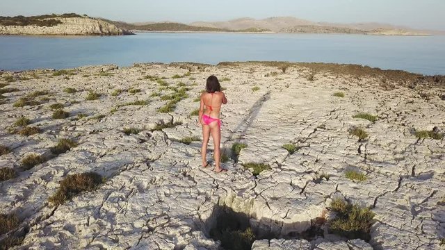 A sexy woman in a bikini talking on a cell phone on a small round shaped island at Kornati Croatia. An orbit shot with a drone.