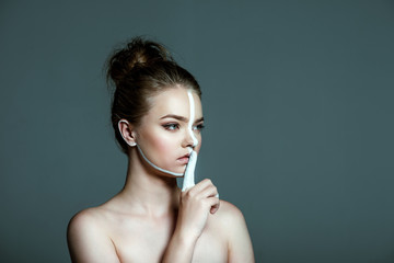young beautiful teen girl with creative white body art line on face showing shh sign, isolated on grey, silence concept