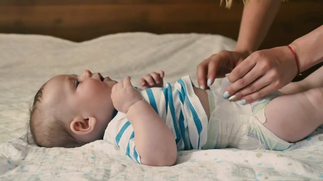 The mother changes the diaper of the baby on the bed