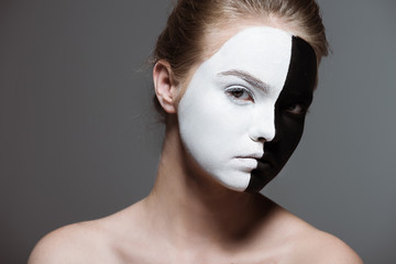 young stylish girl with creative white and black bodyart on face looking at camera, isolated on grey