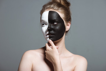 young pensive girl with creative white and black bodyart on face, isolated on grey