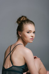 attractive blonde teenage girl in leotard looking at camera, isolated on grey