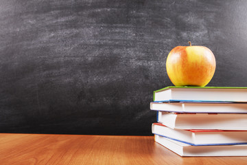 A stack of books and an apple on blackboard background with copyspace for your text, design. Back to school concept for banner, promotion, web