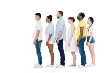 side view of young multiethnic people standing in row and smiling at camera isolated on white