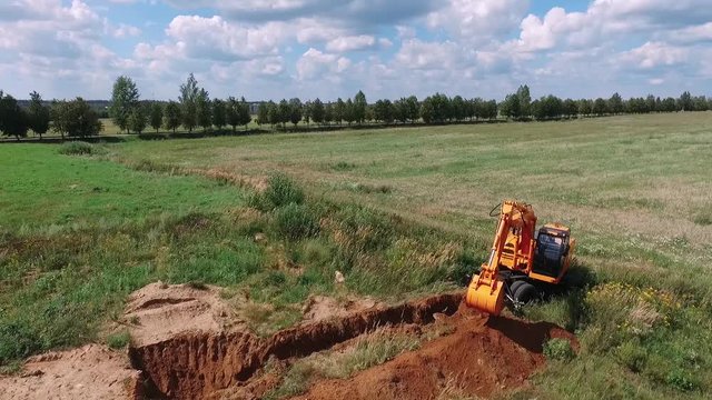 Excavator digs the ground in the field, view from height.
