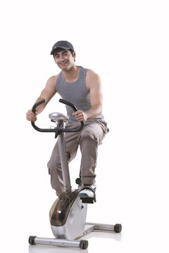 Portrait of a young man on exercise bike over white background 