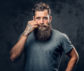 A man touches his moustache over grey background.