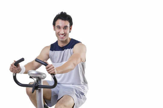 Portrait of a happy young man on exercise bike over white background 