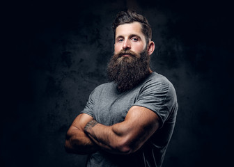 Bearded male with tattoos on arms over grey background.