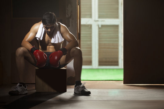 Tired young male boxer sitting on stool in gym