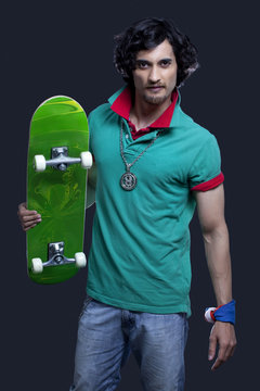 Portrait of a funky young man holding skateboard against black background 