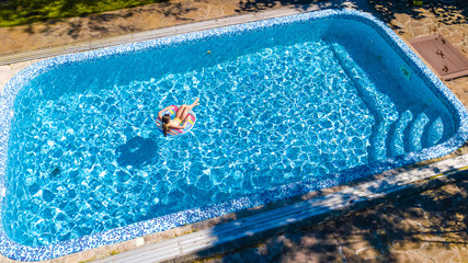 Aerial view of girl in swimming pool from above, kid swim on inflatable ring donut and has fun in water on family vacation
