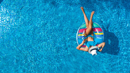 Aerial view of beautiful girl in swimming pool from above, swim on inflatable ring donut and has fun in water on family vacation
