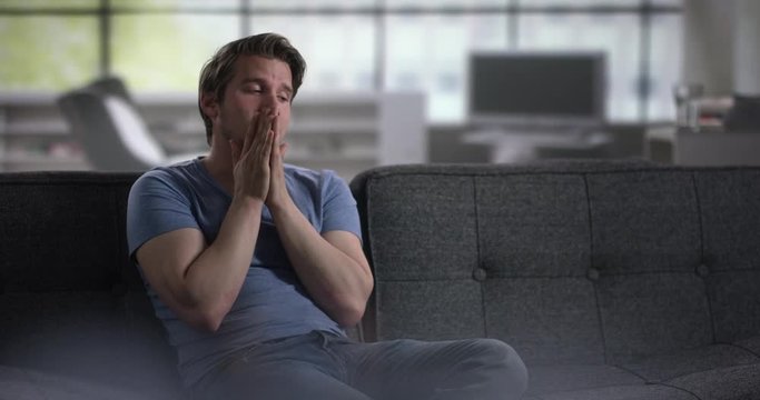 Depressed young man on a couch throwing his hands in dispair