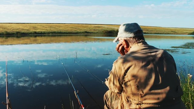 The jerboa sits on the shore of the lake and waits for a bite. Fishing rods are thrown into the water and fish. A picturesque place on the shore of the reservoir. Fish does not bite. Smooth calm calm