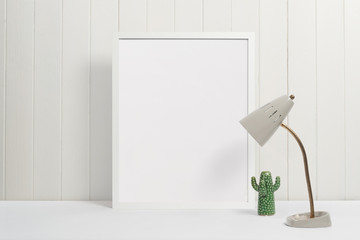 White picture frame on white background with lamp and green cactus