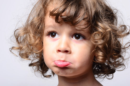 Portrait of a beautiful sad boy. Toddler feeling sadness because he was disappointed. Adorable boy having different emotions. Kid making funny faces. Boy with long curly hair.