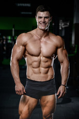 Fototapeta na wymiar Muscular handsome athletic bodybuilder fitness model posing after exercises in gym on diet .