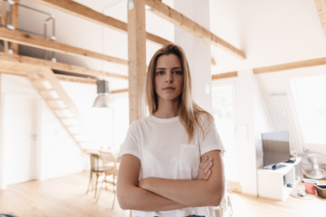 Confident young woman standing in her apartment with arms crossed