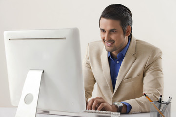 Naklejka premium Happy young businessman using computer at office desk