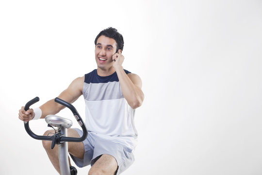 Young man exercising while talking on cell phone over white background 