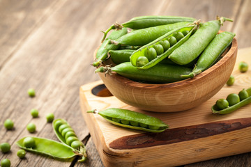 Ripe peas in a wooden bowl on wooden table