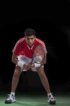 Full length portrait of young male player playing tennis over black background